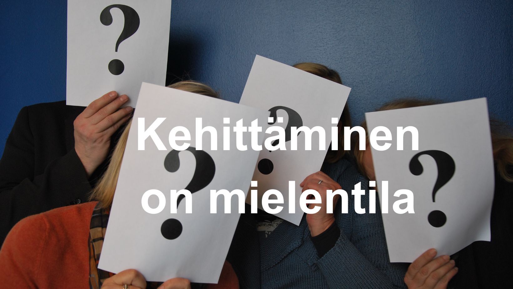 ihmisiä, joilla on käsissään A4:lla suuria kysymysmerkkejä, teksti: kehittäminen on mielentila.